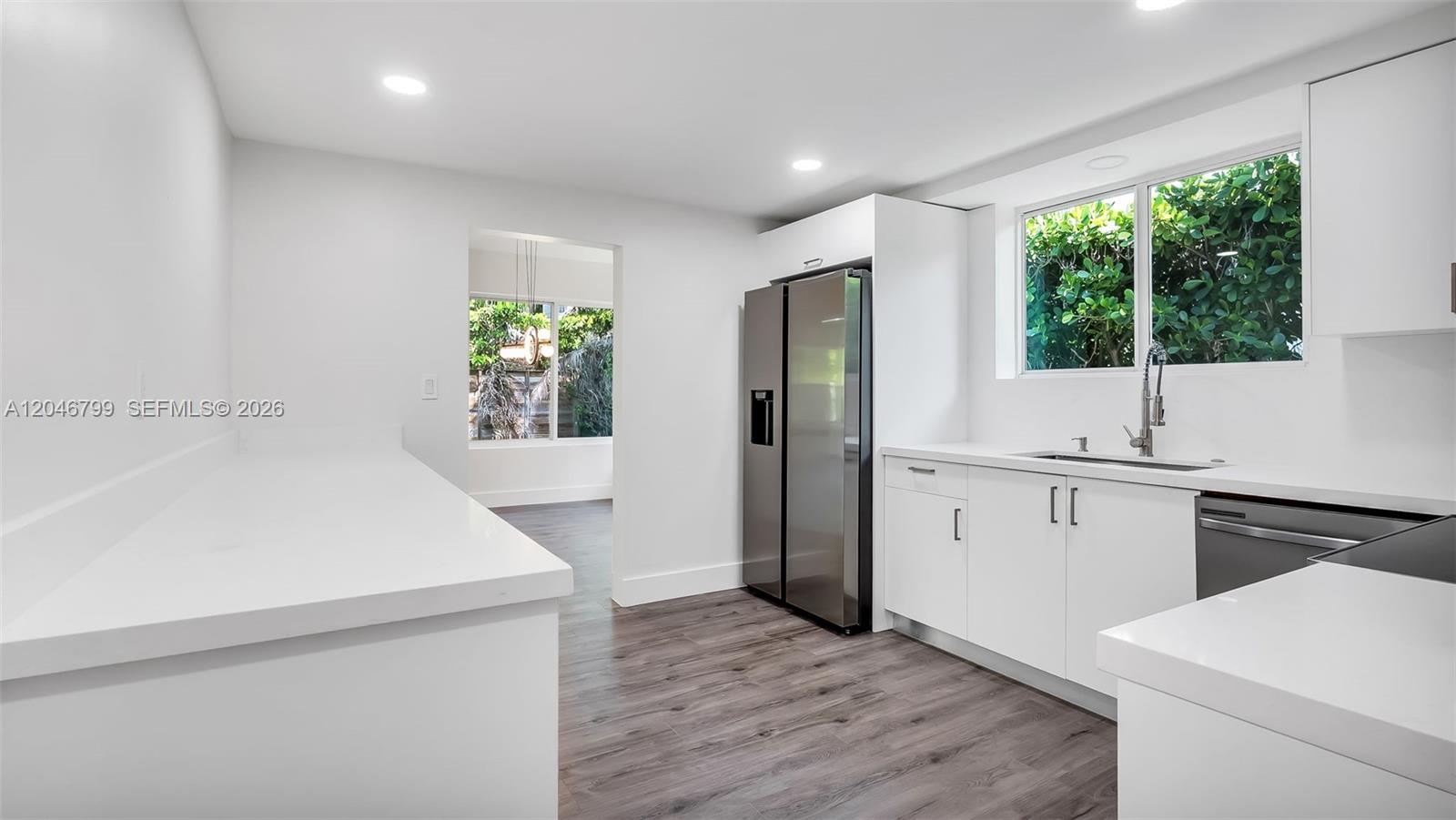 A modern kitchen features white cabinets, stainless steel appliances, and dark wood-look flooring — 1500 NE 13th Pl, Miami FL 33139, MIAMI, FL