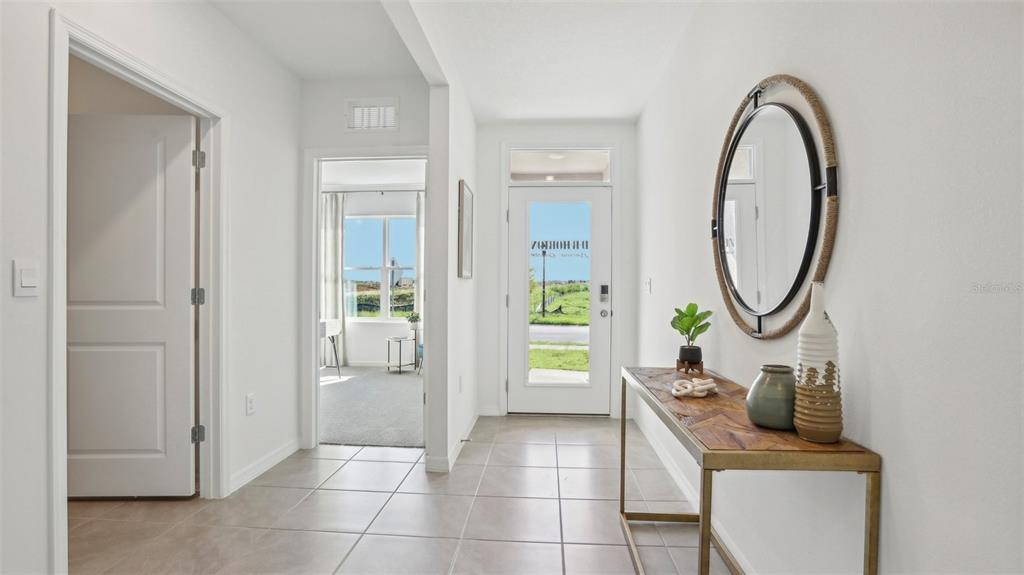 A tiled entryway features a console table, a round mirror, and a view into a room — 13609 NEW JADE AVENUE, WIMAUMA, FL