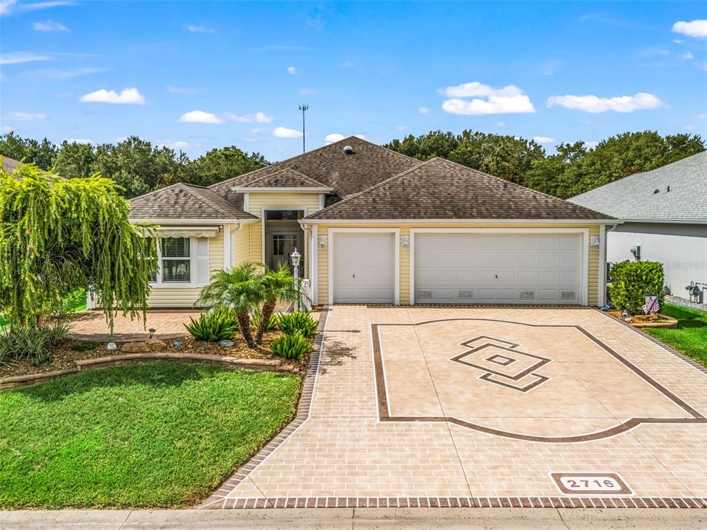 A single-story house with yellow siding, a three-car garage, and a decorative paved driveway — 2716 LYALL LOOP, THE VILLAGES, FL