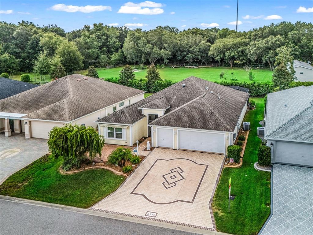 An aerial view shows a suburban house with a decorative paved driveway and green lawn — 2716 LYALL LOOP, THE VILLAGES, FL
