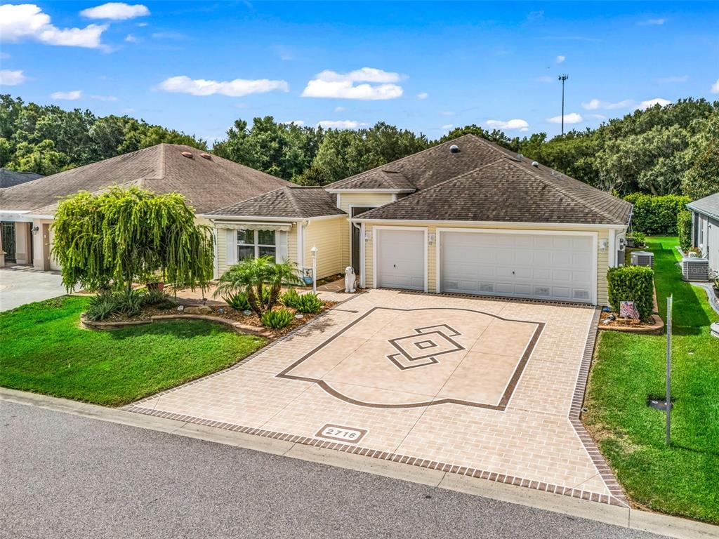 A single-story house with a decorative paved driveway, a two-car garage, and a landscaped front yard — 2716 LYALL LOOP, THE VILLAGES, FL