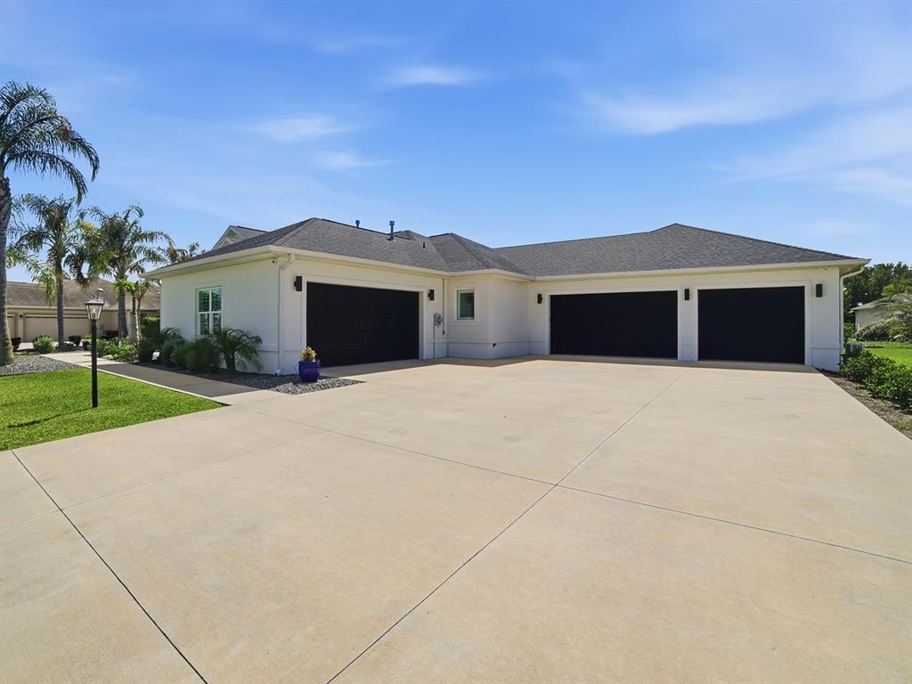A house exterior features a large concrete driveway and three black garage doors — 858 PINCKNEY LANE, THE VILLAGES, FL