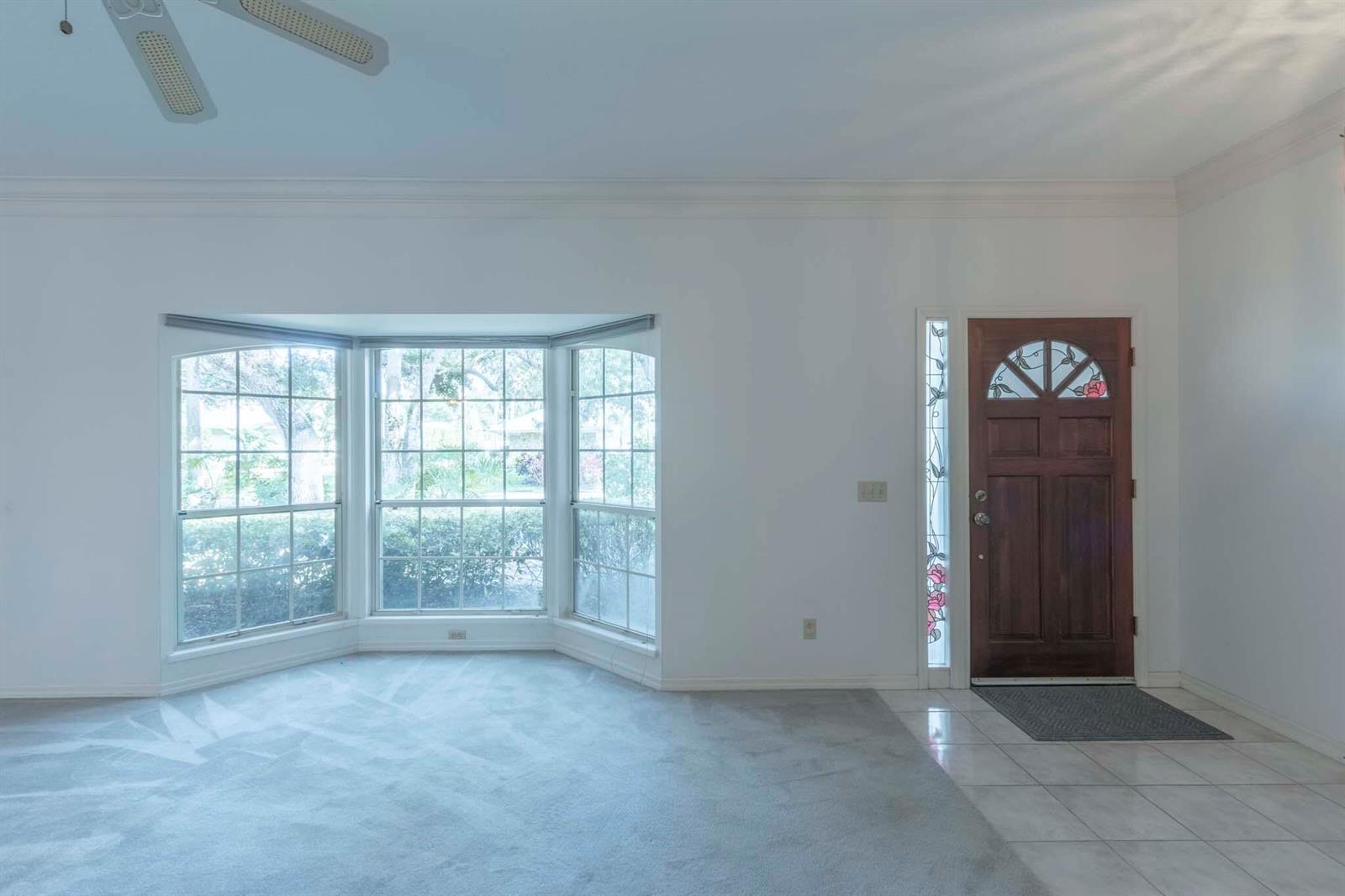 A living room with a bay window, carpeted flooring, and a wooden front door — 1027 Mangrove Lane, Vero Beach FL 32963, VERO BEACH, FL