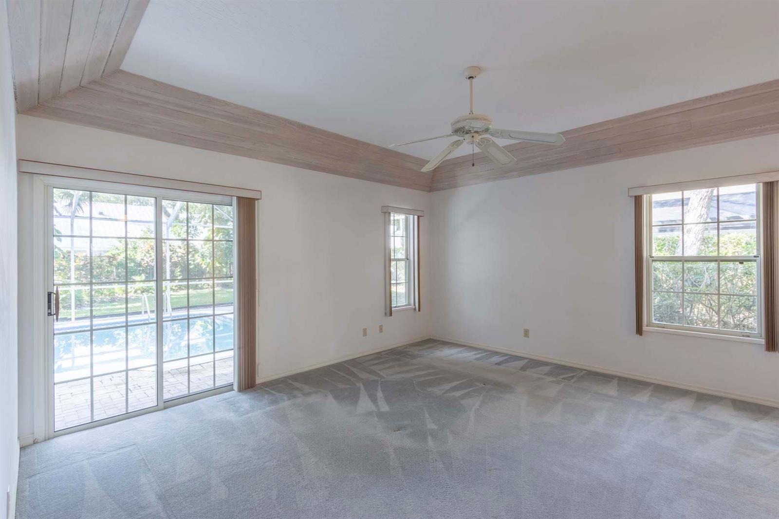 An empty bedroom with gray carpet, a tray ceiling, and sliding glass doors to a pool — 1027 Mangrove Lane, Vero Beach FL 32963, VERO BEACH, FL