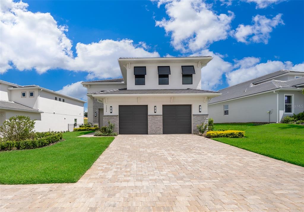 A two-story house with a paved driveway, two garage doors, and white stucco siding — 16046 VOLTERRA POINT, BELLA COLLINA, FL