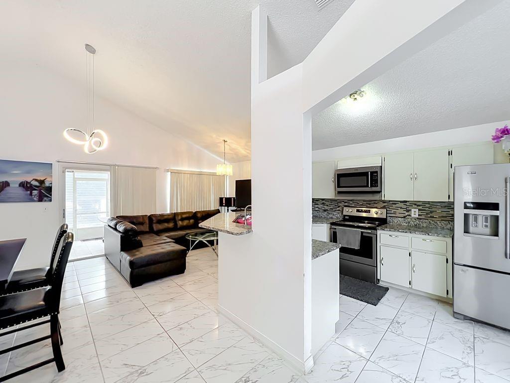 A kitchen with white cabinets and marble-look tile floors opens into a living room area — 3549 SPRING LAND DRIVE, ORLANDO, FL