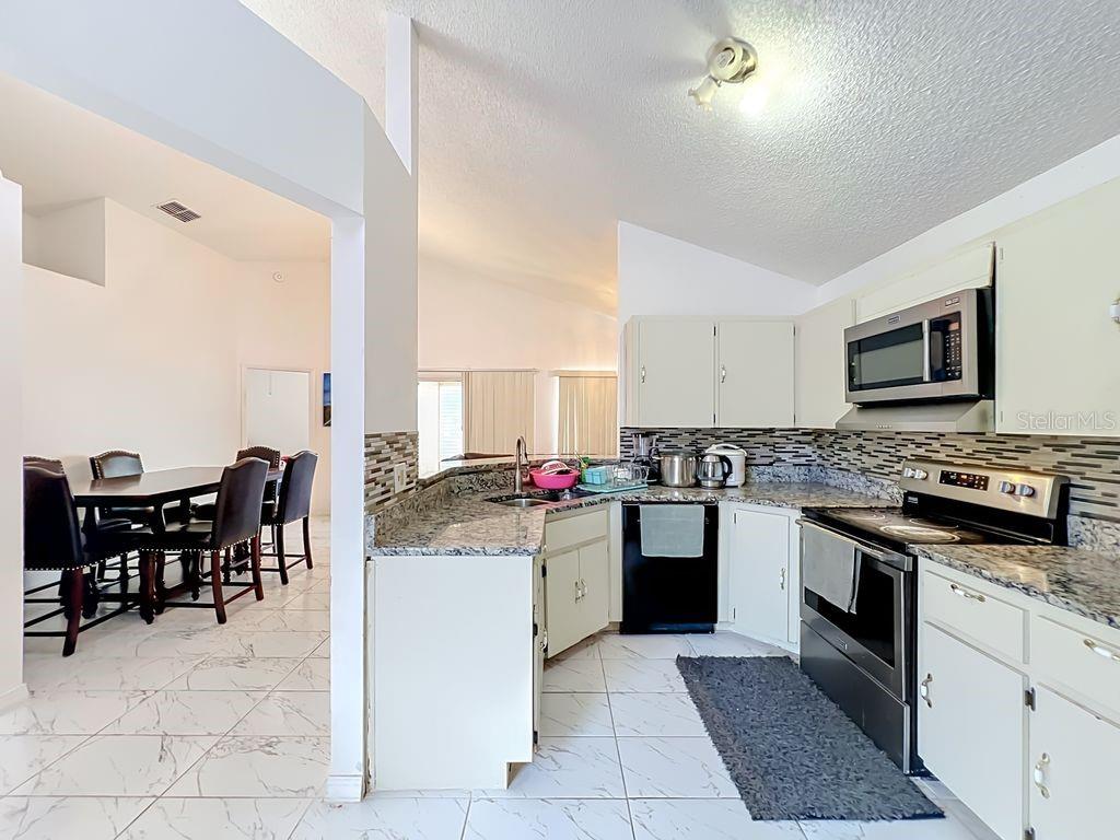 A kitchen with white cabinets, granite countertops, and tile flooring opens to a dining area — 3549 SPRING LAND DRIVE, ORLANDO, FL