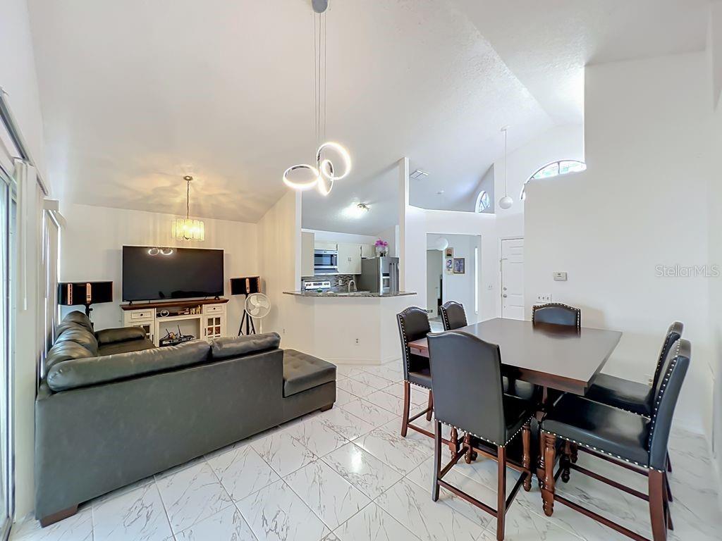 An open-concept living and dining area features white tile floors, vaulted ceilings, and modern lighting — 3549 SPRING LAND DRIVE, ORLANDO, FL
