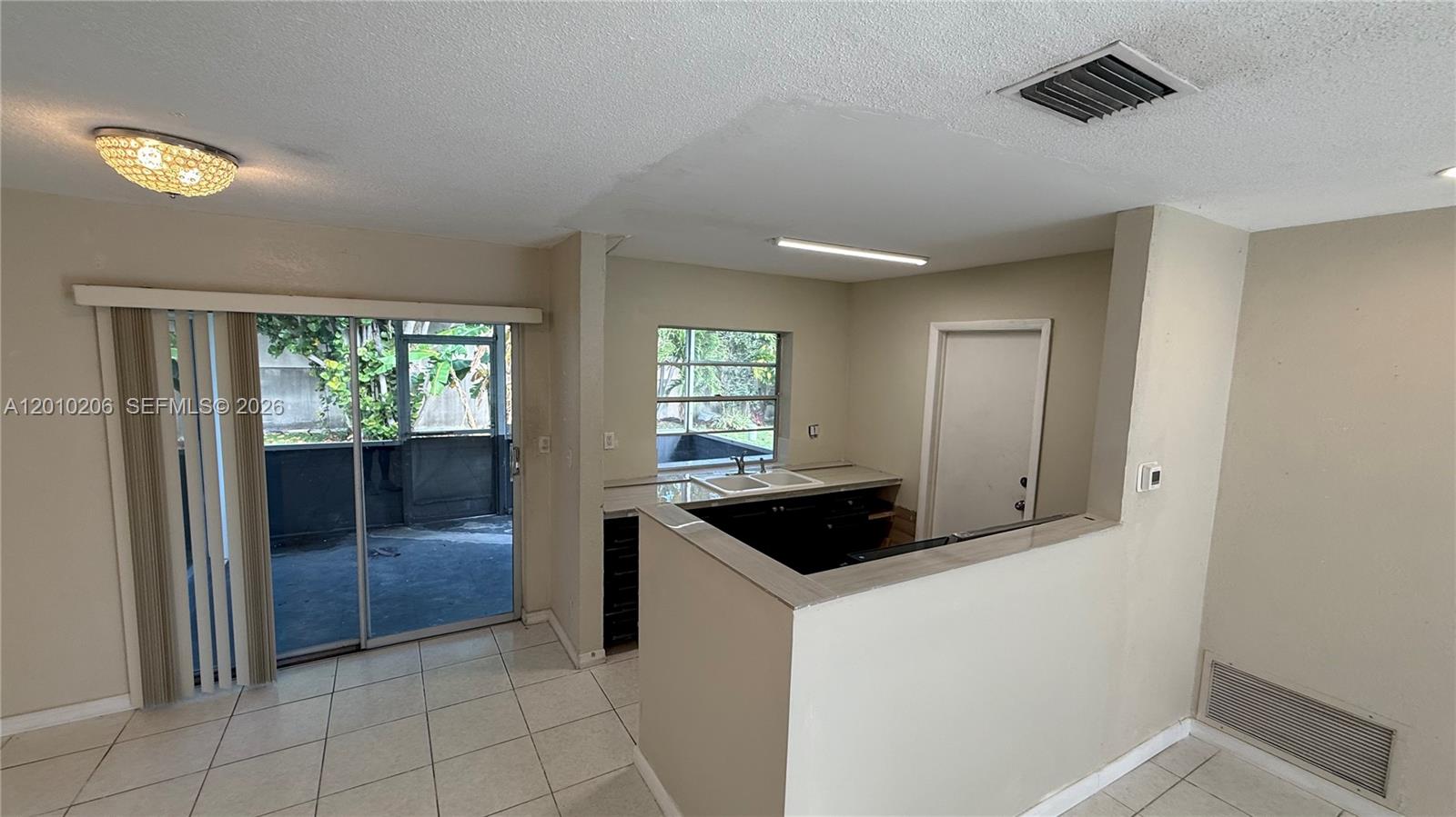 A kitchen with dark cabinets and a sink overlooks a tiled dining area and patio — 3021 NW 2nd Ave, Pompano Beach FL 33064, POMPANO BEACH, FL