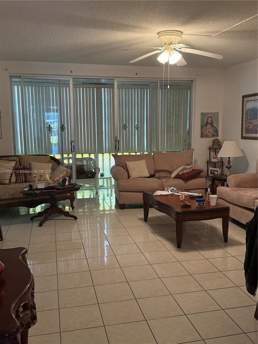 A living room features light-colored tile flooring, beige upholstered furniture, and large sliding glass doors — 18555 NE 14th Ave # B, Miami FL 33179, MIAMI, FL