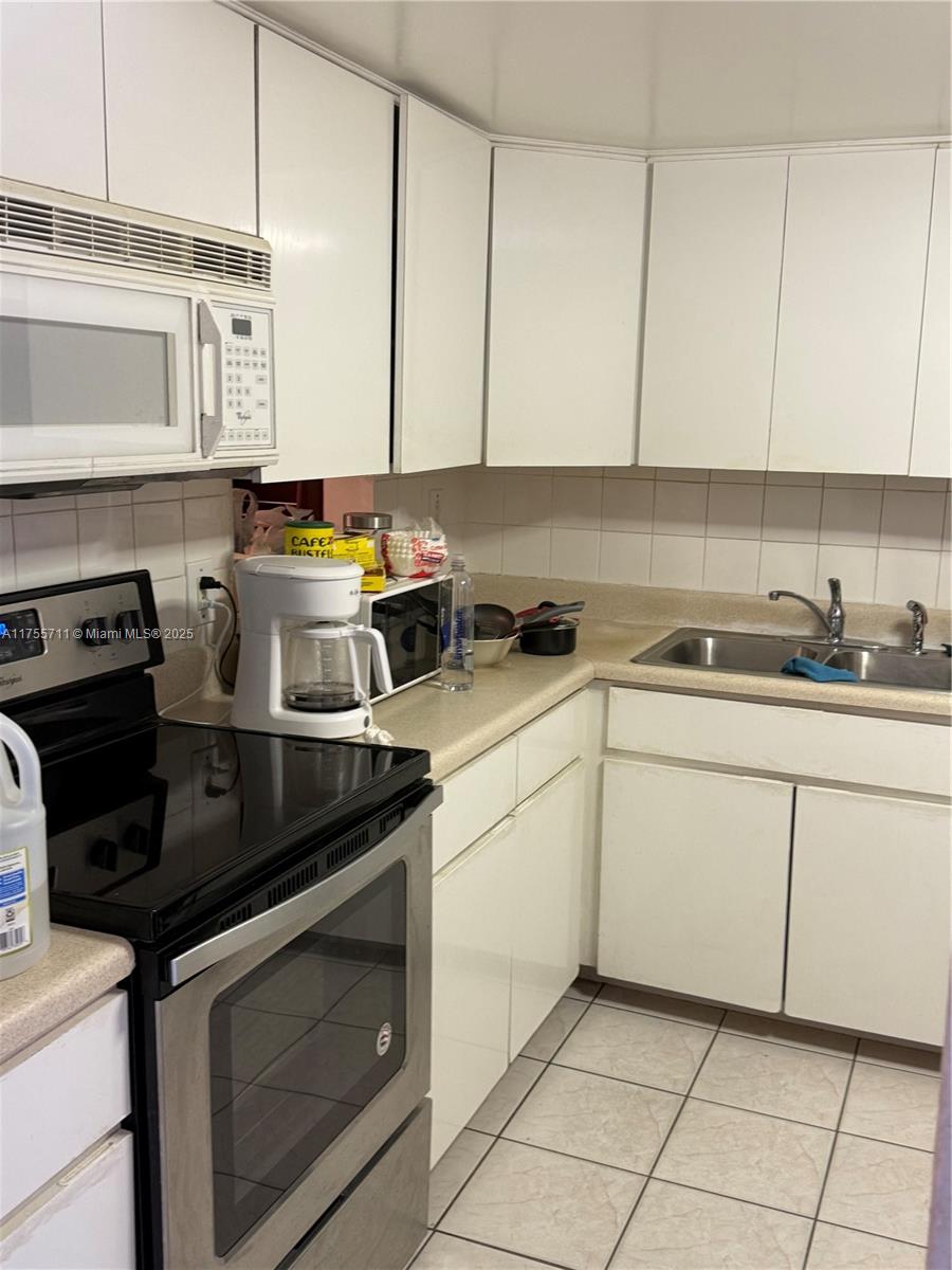 A kitchen features white cabinets, a black stove, a microwave, and a stainless steel sink — 18555 NE 14th Ave # B, Miami FL 33179, MIAMI, FL