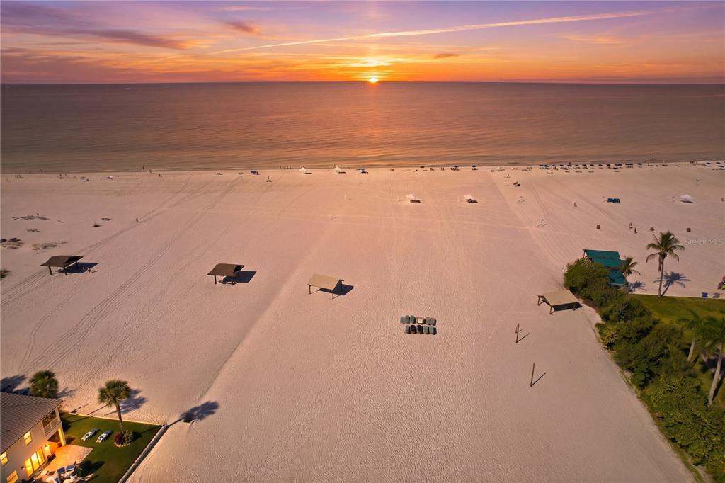 An aerial view shows a sandy beach at sunset with several cabanas and palm trees — 6006 MIDNIGHT PASS ROAD UNIT 48, SARASOTA, FL