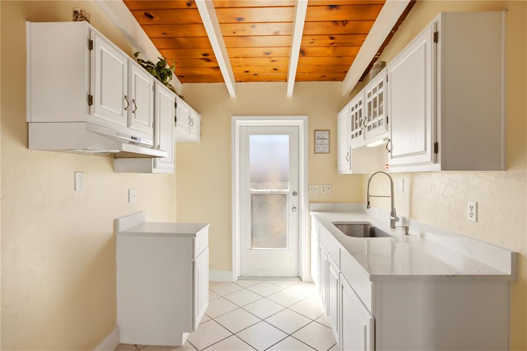 A galley kitchen features white cabinets, white countertops, a wood-paneled ceiling, and tiled floors — 6006 MIDNIGHT PASS ROAD UNIT 48, SARASOTA, FL