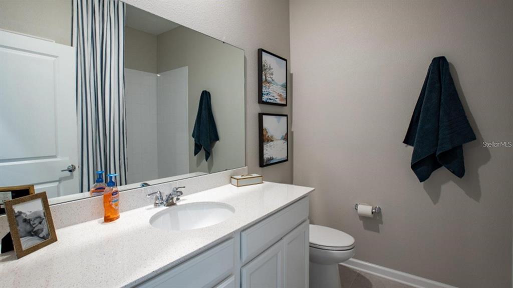A bathroom features a white vanity with a quartz countertop, a large mirror, and a toilet — 643 GROVE STREET, WINTER HAVEN, FL
