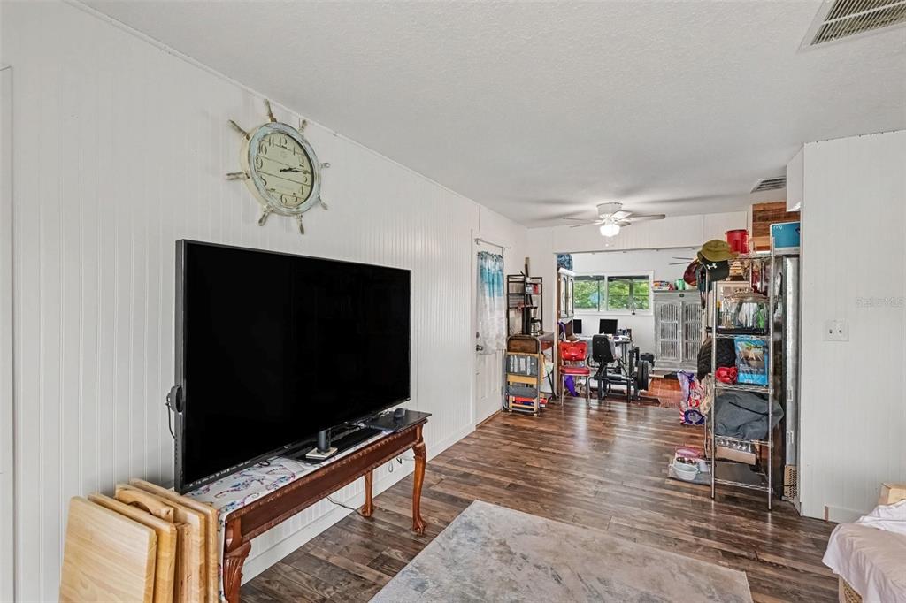 A living room features a large television on a wooden table, wood-look flooring, and white walls — 2731 PINE RIDGE DRIVE, TITUSVILLE, FL
