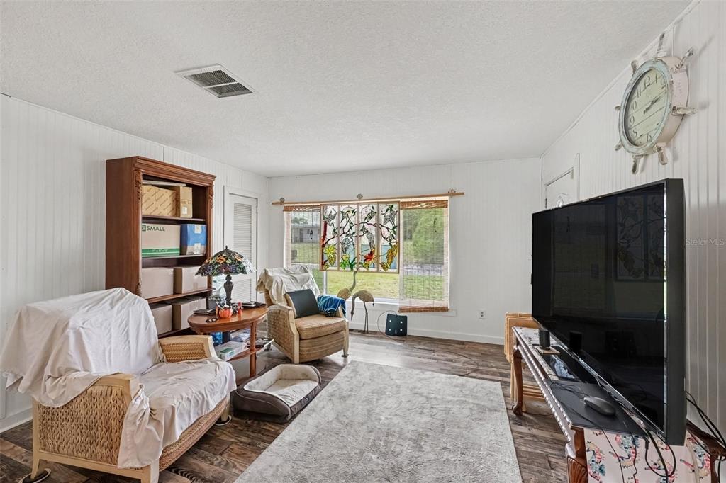 A living room features white paneled walls, a stained glass window, and a large television — 2731 PINE RIDGE DRIVE, TITUSVILLE, FL