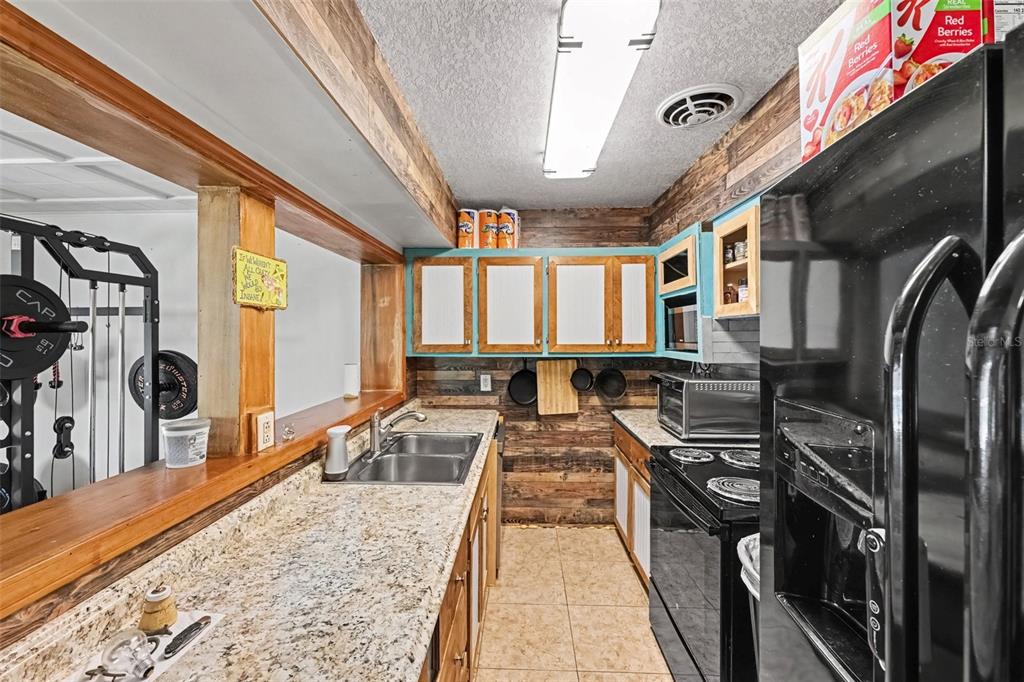 A kitchen features granite countertops, wood-paneled walls, teal-trimmed cabinets, and a black refrigerator — 2731 PINE RIDGE DRIVE, TITUSVILLE, FL