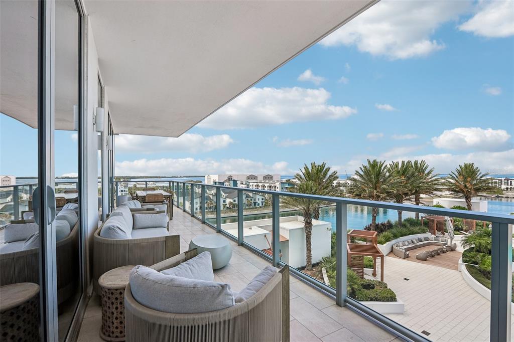 A balcony with outdoor seating overlooks a swimming pool, palm trees, and a body of water — 5120 MARINA WAY UNIT 7703, TAMPA, FL