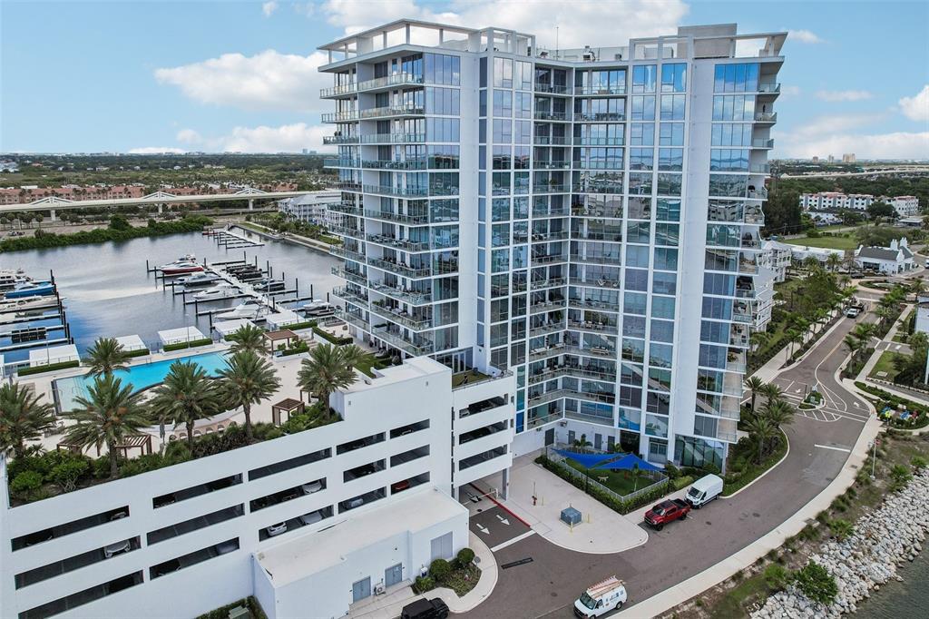 An aerial view shows a modern high-rise apartment building with an adjacent pool and marina — 5120 MARINA WAY UNIT 7703, TAMPA, FL
