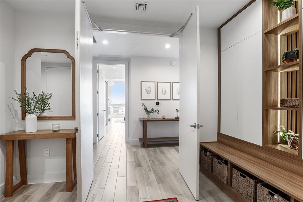 A modern entryway features wood-toned console tables, built-in storage, and light-colored wood-look tile flooring — 5120 MARINA WAY UNIT 7703, TAMPA, FL