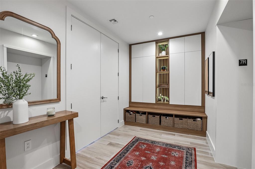 A modern entryway features a wooden bench with storage baskets, built-in cabinetry, and a mirror — 5120 MARINA WAY UNIT 7703, TAMPA, FL