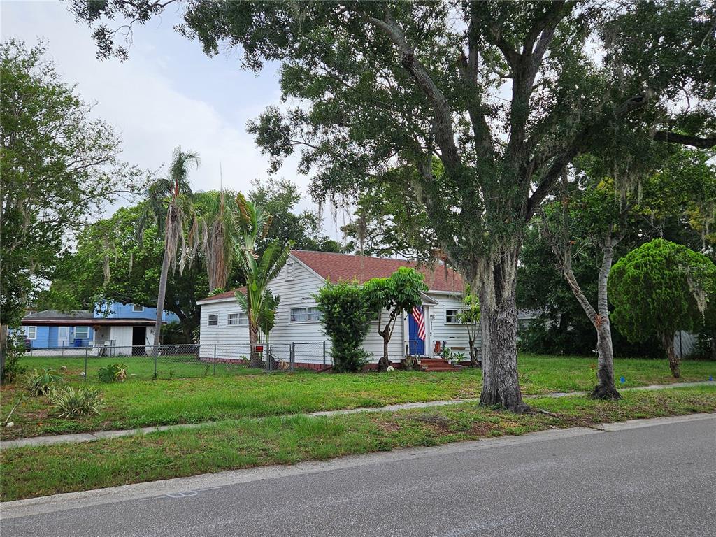 A white, single-story house with a red roof sits behind a chain-link fence — 4605 8TH AVENUE N, ST PETERSBURG, FL