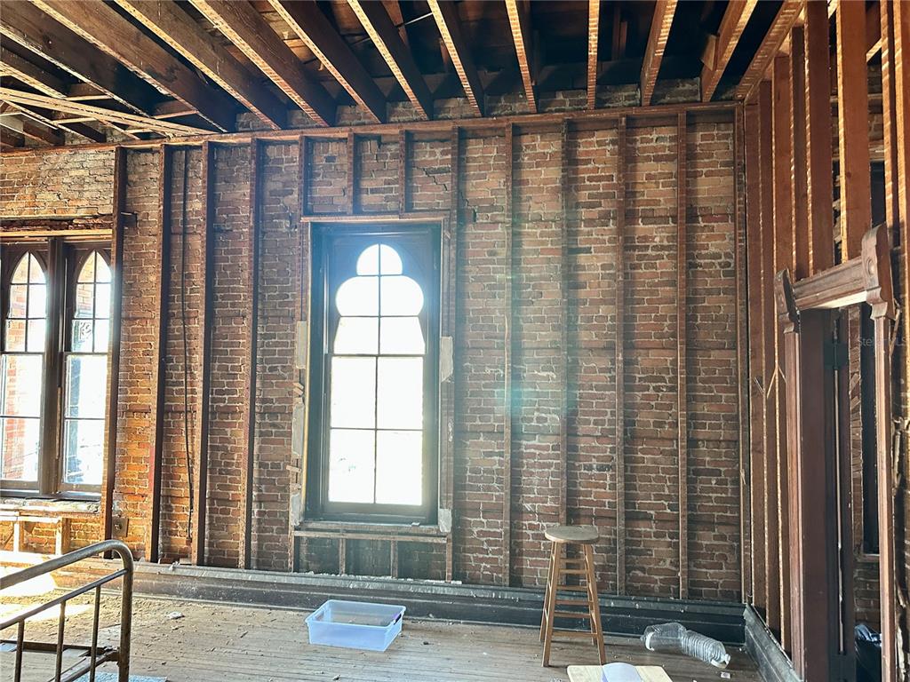 An interior room under renovation features exposed brick walls, wood framing, and arched windows — 209 N OAK AVENUE, SANFORD, FL