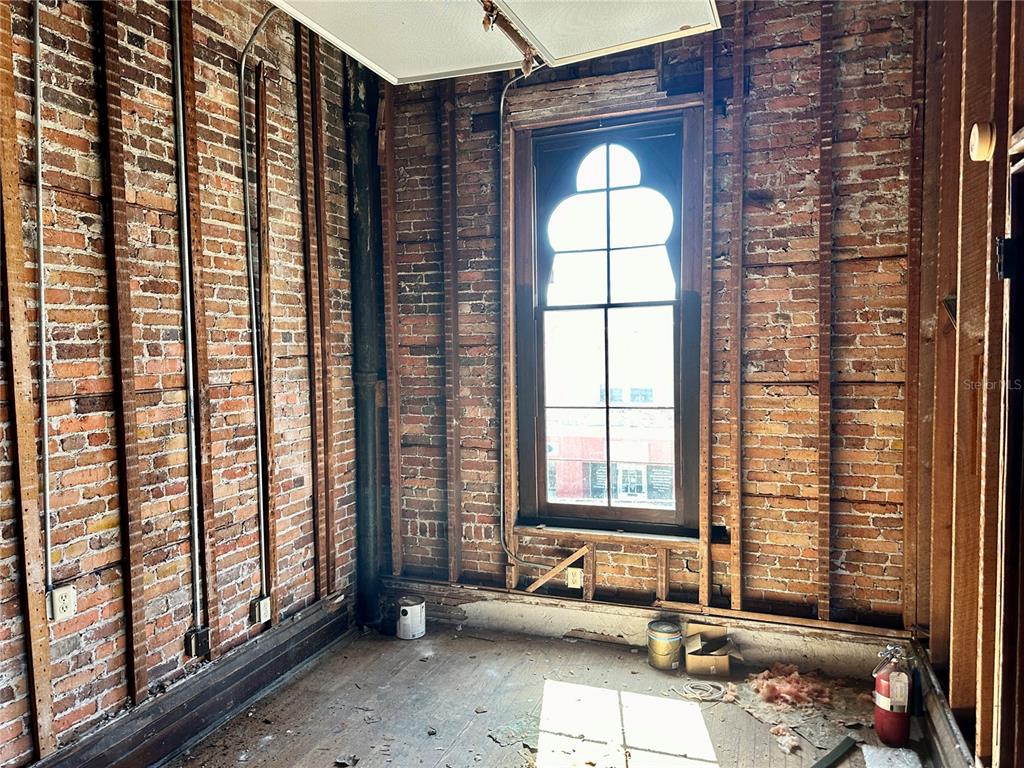 An unfinished room features exposed brick walls, wooden studs, and a unique arched window — 209 N OAK AVENUE, SANFORD, FL