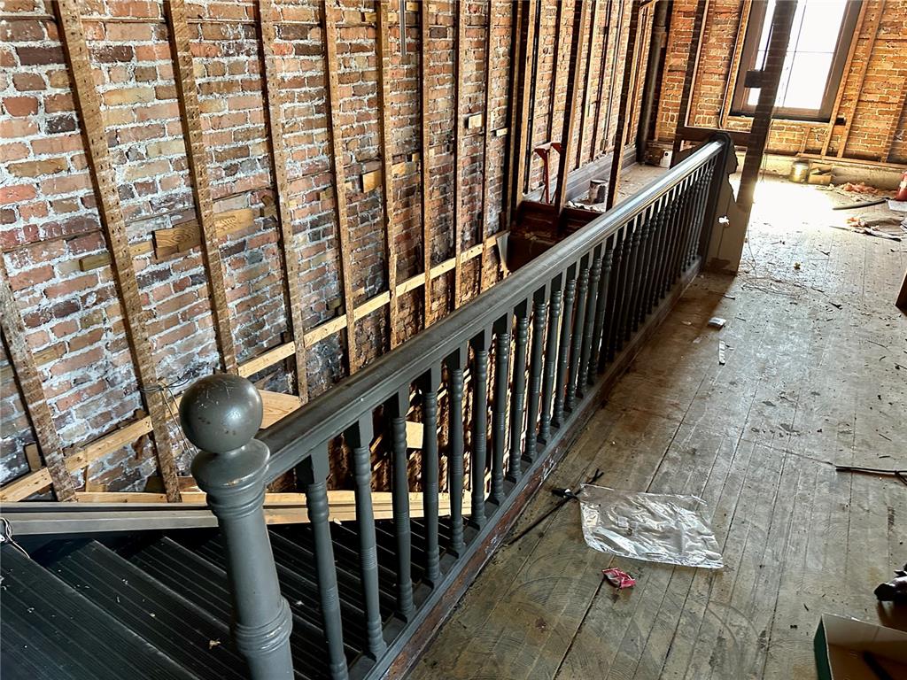 A staircase with a dark railing overlooks a room with exposed brick walls and wood flooring — 209 N OAK AVENUE, SANFORD, FL
