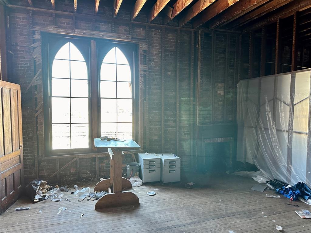 An unfinished room features exposed brick walls, arched windows, and wooden ceiling joists — 209 N OAK AVENUE, SANFORD, FL