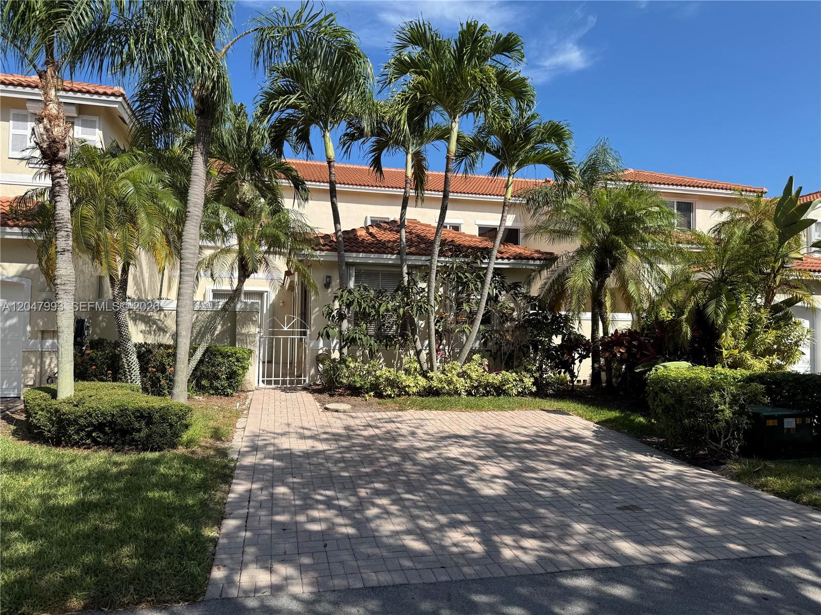 A two-story townhouse features a brick paver driveway, palm trees, and a tile roof — 1595 Seagrape Way, Hollywood FL 33019, HOLLYWOOD, FL