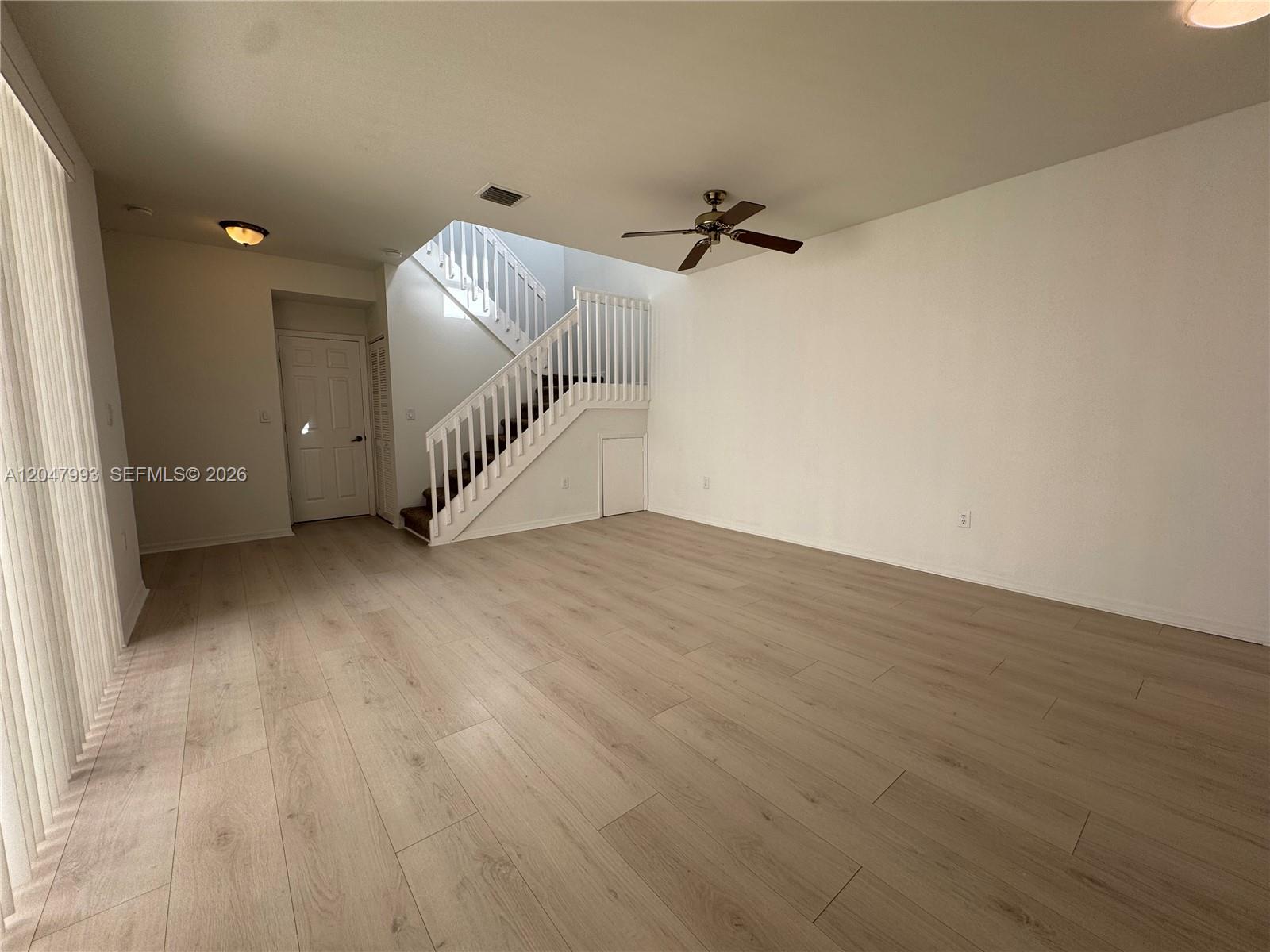 An empty living room features light wood-look flooring, a ceiling fan, and a staircase — 1595 Seagrape Way, Hollywood FL 33019, HOLLYWOOD, FL