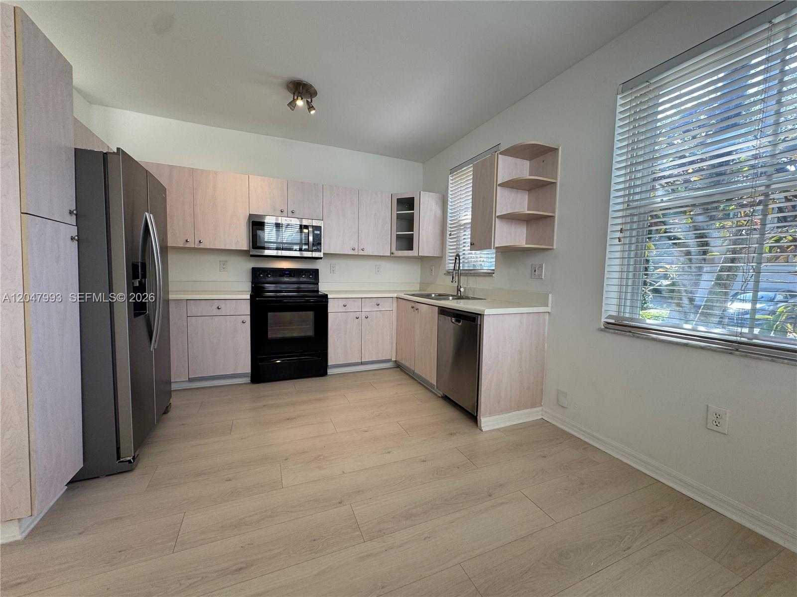 A kitchen features light wood cabinets, stainless steel appliances, and light-colored laminate flooring — 1595 Seagrape Way, Hollywood FL 33019, HOLLYWOOD, FL