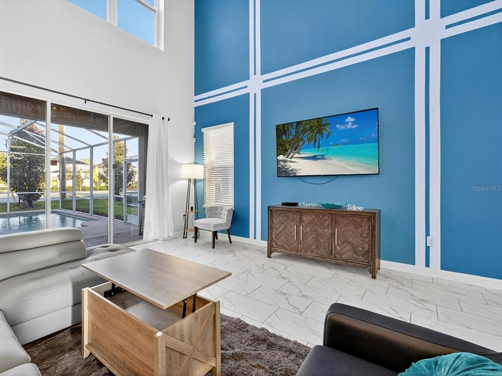 A living room features a blue accent wall with white trim, tile flooring, and pool views — 620 STICKS STREET, DAVENPORT, FL