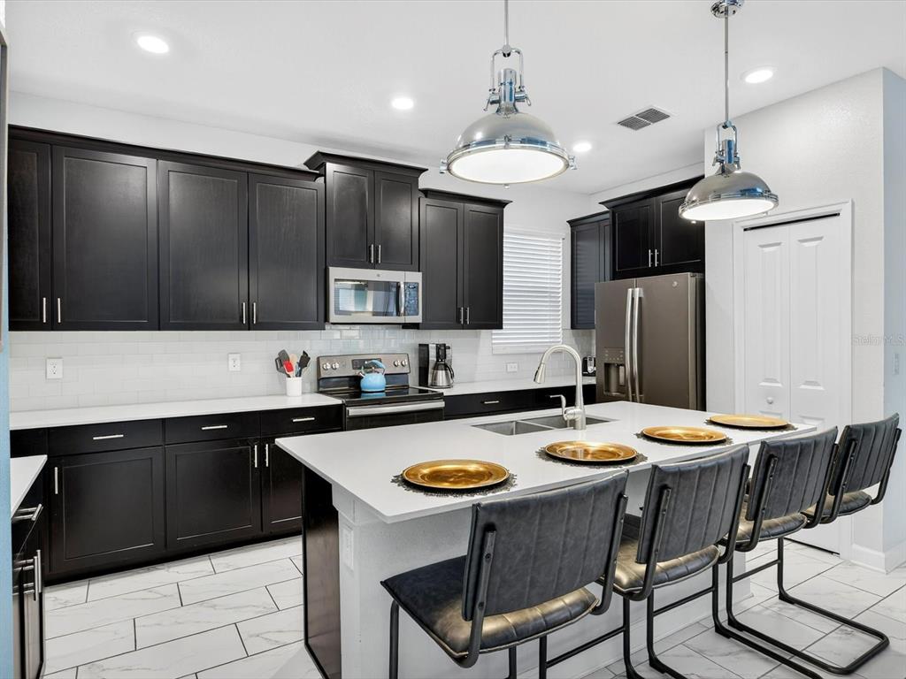 A modern kitchen features dark cabinets, white countertops, a large island, and stainless steel appliances — 620 STICKS STREET, DAVENPORT, FL