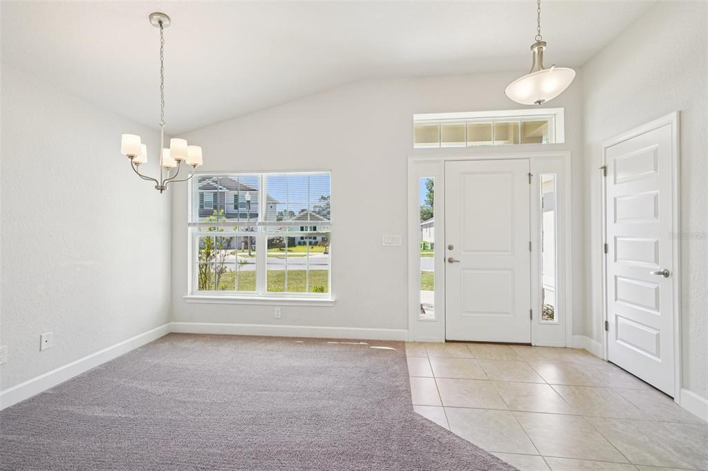 A dining area with carpeted flooring, a chandelier, and an adjacent tiled entryway with a door — 4588 SE 25TH LOOP, OCALA, FL