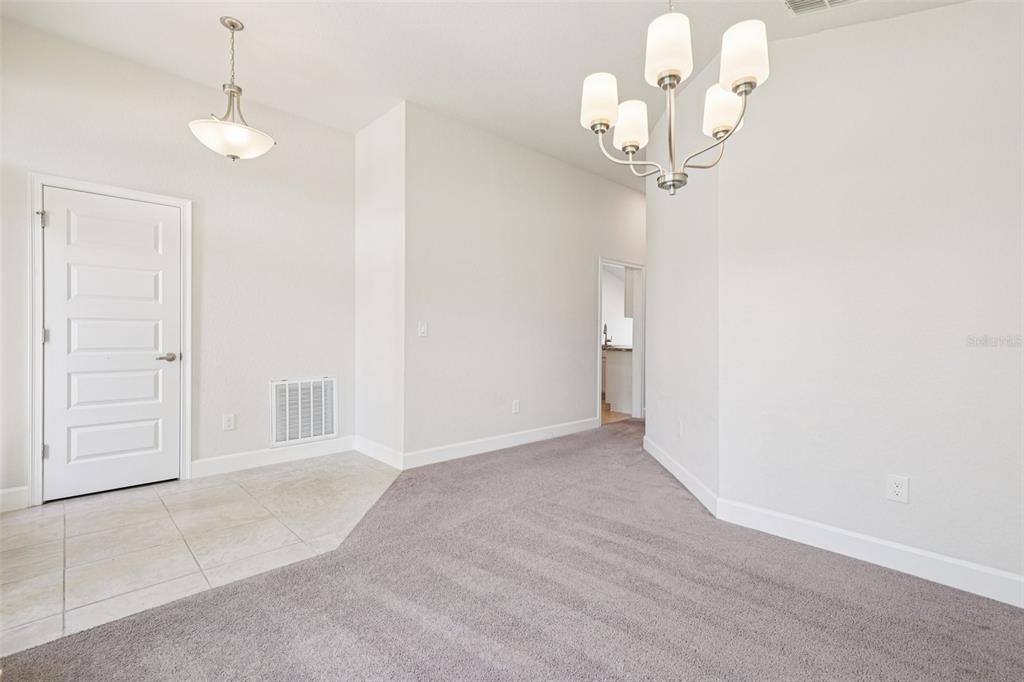A dining area features a chandelier, carpeted flooring, a tiled entryway, and a white door — 4588 SE 25TH LOOP, OCALA, FL