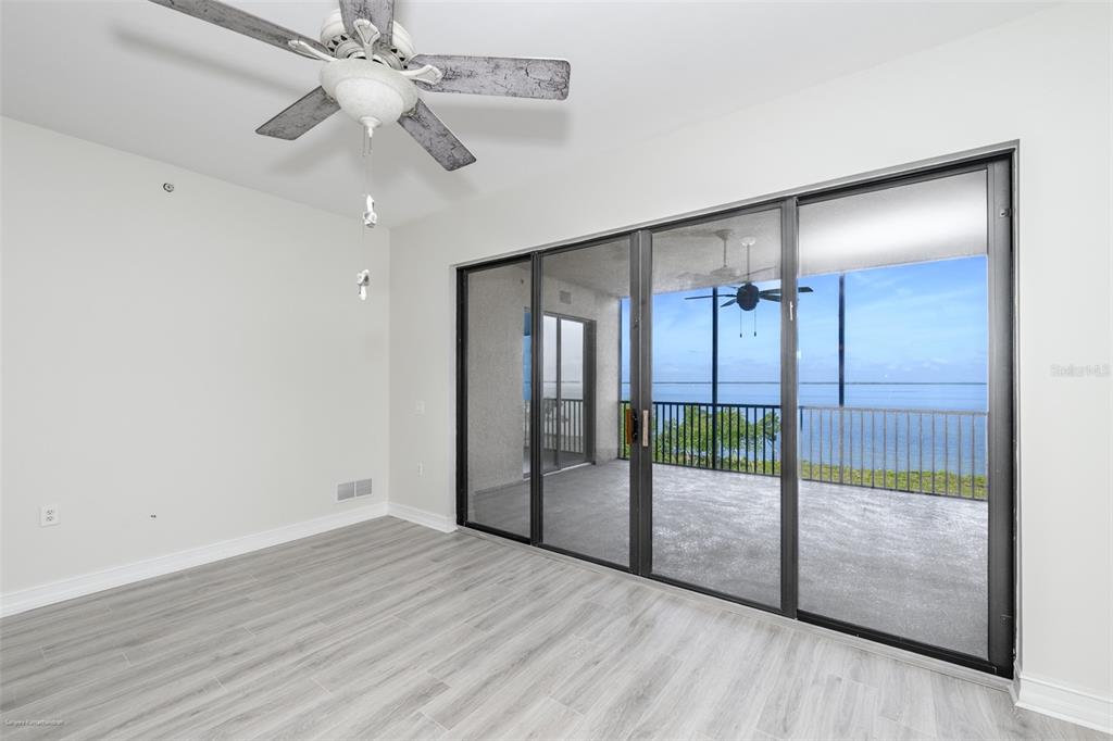 An empty room with light wood-look flooring, a ceiling fan, and sliding doors to a balcony — 89 VIVANTE BOULEVARD UNIT 402, PUNTA GORDA, FL