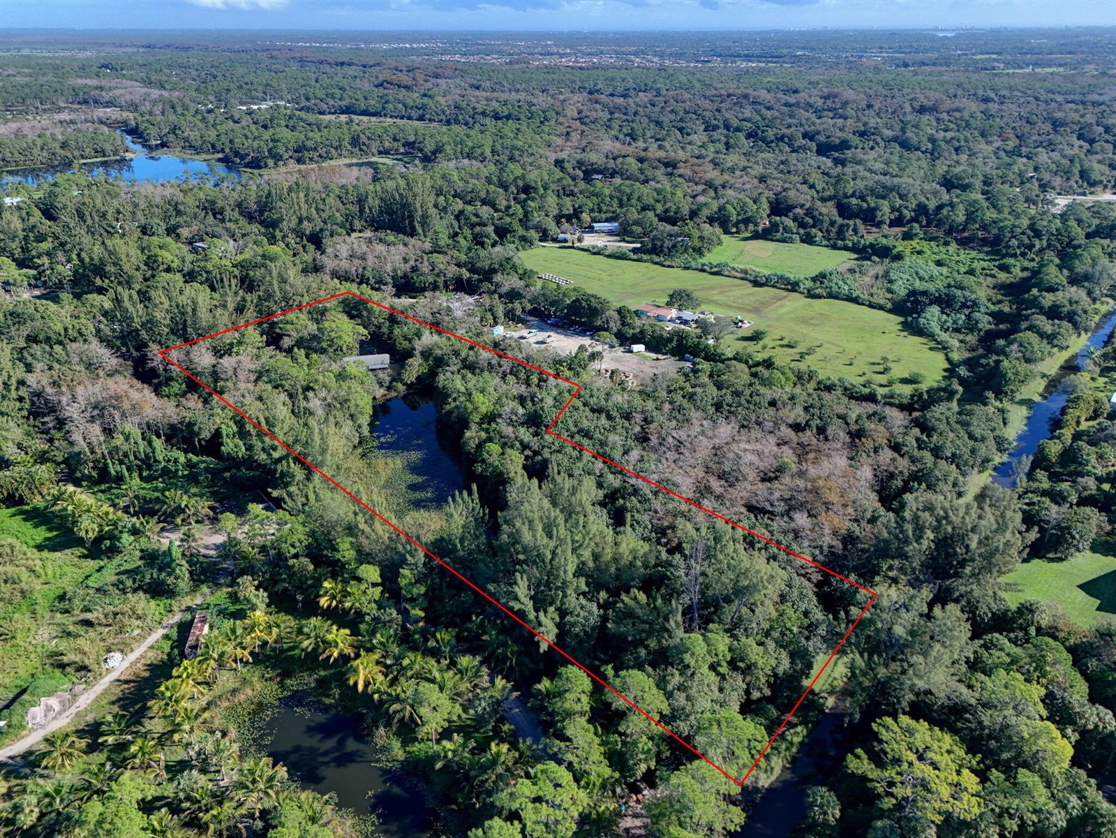 An aerial view shows a wooded lot with a pond outlined in red — 9620 171st Street N, Jupiter FL 33478, JUPITER, FL