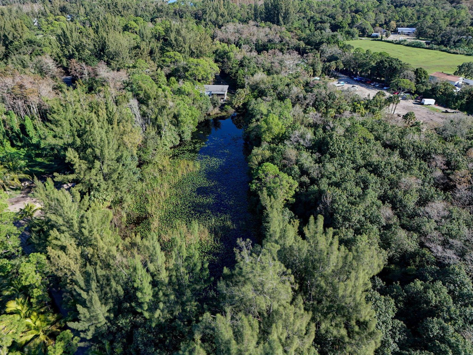 An aerial view shows a narrow pond surrounded by dense forest and nearby parking areas — 9620 171st Street N, Jupiter FL 33478, JUPITER, FL