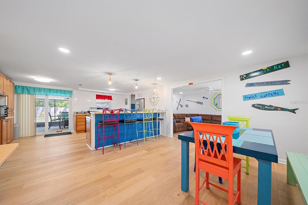A bright, open-concept kitchen and dining area features colorful chairs and light wood flooring — 2923 LINWOOD DRIVE, SARASOTA, FL