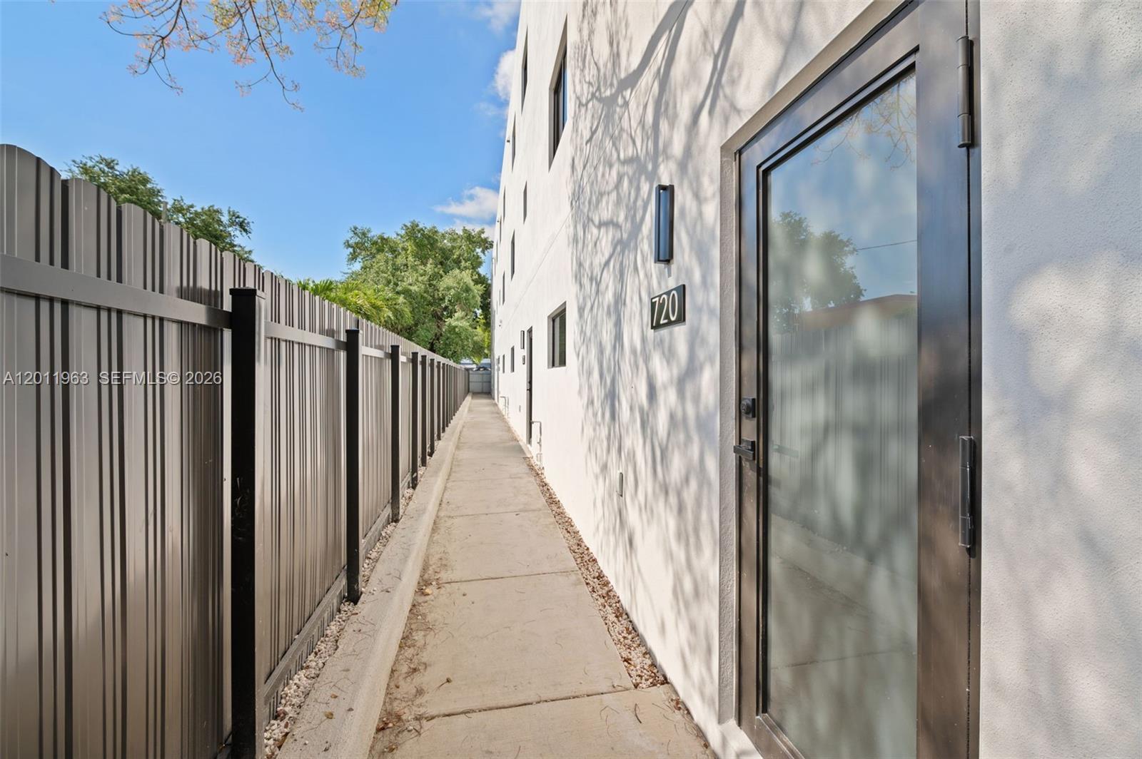 A narrow concrete walkway runs between a metal fence and a white building exterior — 720 NW 55th Ter # 720, Miami FL 33127, MIAMI, FL