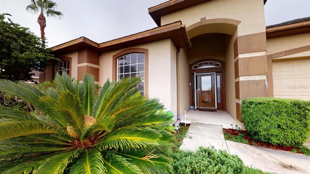 A low-angle exterior view of a house entrance with a palm tree and landscaping — 3552 MACAULEY COURT, OCOEE, FL