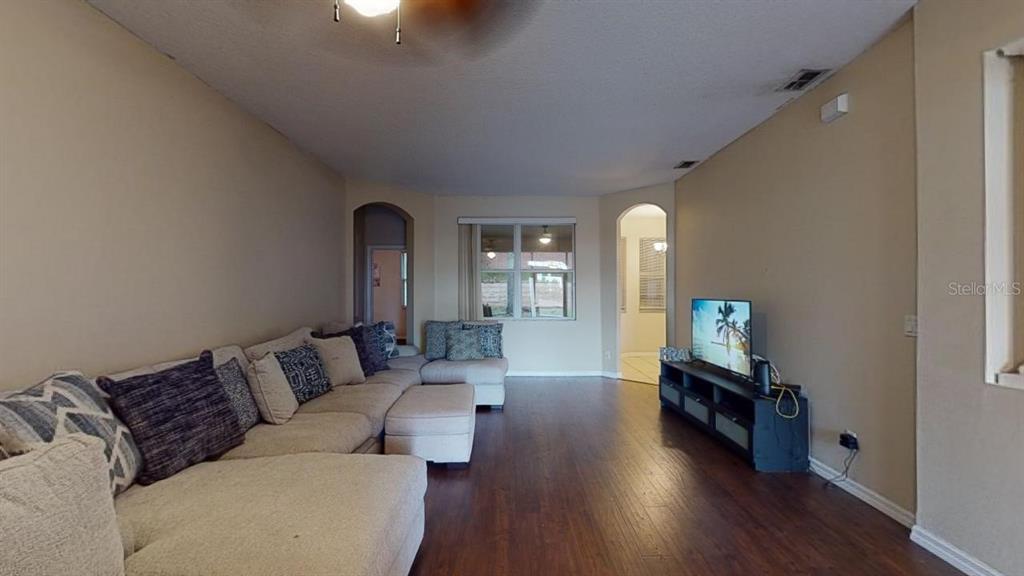A living room features a large sectional sofa, dark wood flooring, and a television console — 3552 MACAULEY COURT, OCOEE, FL