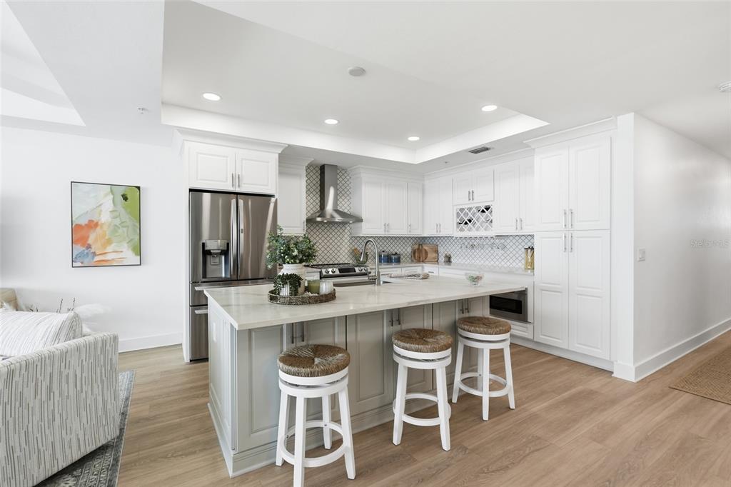 A modern kitchen features white cabinetry, a large gray island with bar stools, and stainless appliances — 1425 PARK BEACH CIRCLE UNIT 1310, PUNTA GORDA, FL