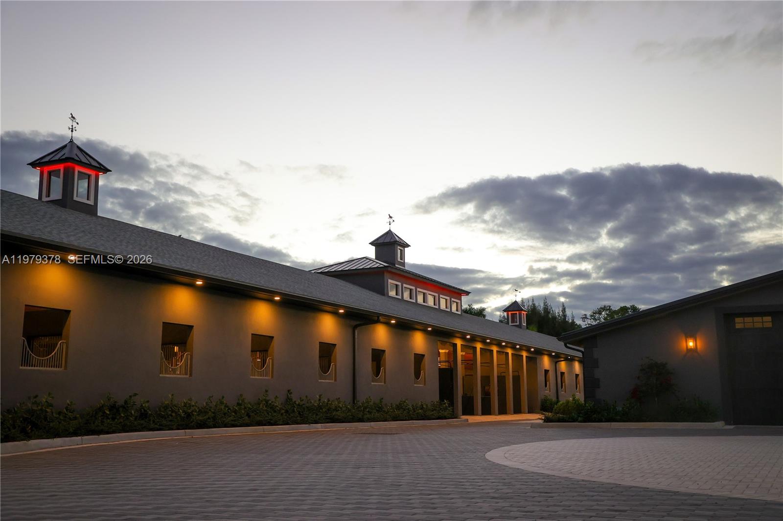 A gray equestrian barn exterior features multiple cupolas, exterior lighting, and a paved circular driveway — 2625 SW 148th Ave, Davie FL 33331, DAVIE, FL