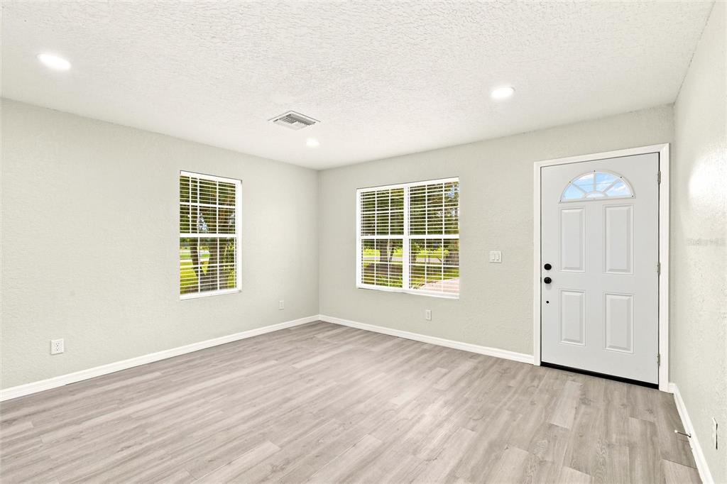 A bright room with light gray walls, wood-look flooring, two windows, and a white door — 2419 SW HILLSBOROUGH AVENUE, ARCADIA, FL