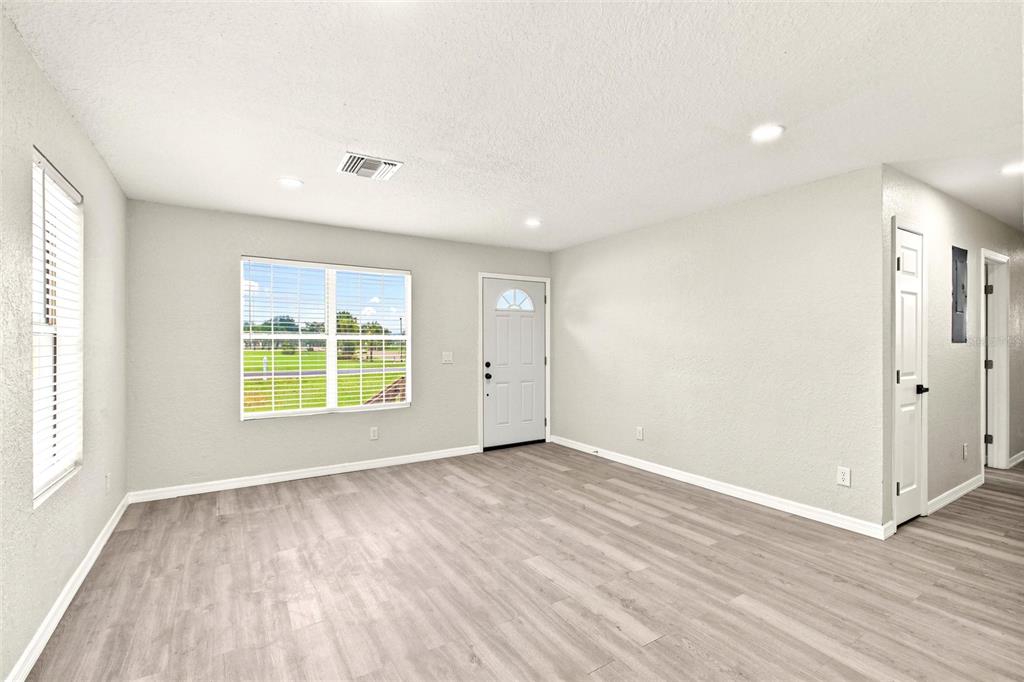 An empty living room features light gray walls, wood-look flooring, a front door, and windows — 2419 SW HILLSBOROUGH AVENUE, ARCADIA, FL