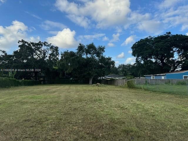 A grassy, vacant lot features mature trees and a chain-link fence under a blue sky — 24xx NW 55 St, Miami FL 33142, MIAMI, FL