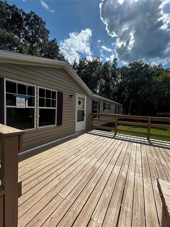 A wooden deck extends from the side of a tan manufactured home with dark shutters — 40838 SUTORUS ROAD, ZEPHYRHILLS, FL